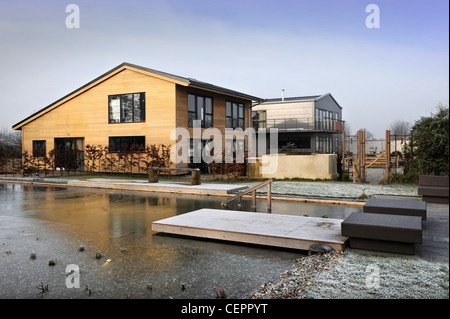 A natural swimming pool which has iced over in winter at a self build wooden clad home UK Stock Photo