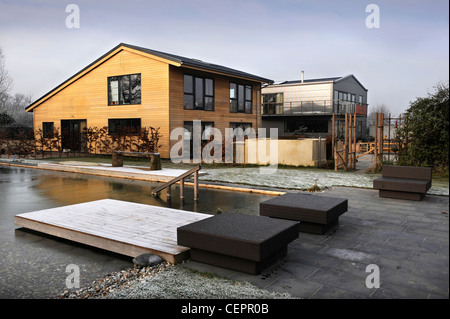 A natural swimming pool which has iced over in winter at a self build wooden clad home UK Stock Photo