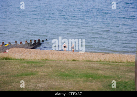 Two women in bathing costumes walking up the pebbled beach away from the sea at Whitstable. Stock Photo