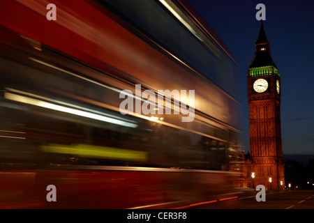 A red double decker bus passing Big Ben at night in Westminster.
