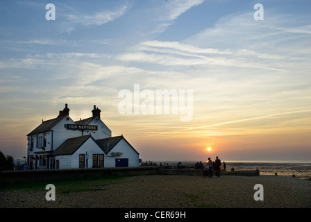 Silhouetted people drinking outside the Neptune pub on the beach at Whitstable in Kent at sunset. Stock Photo