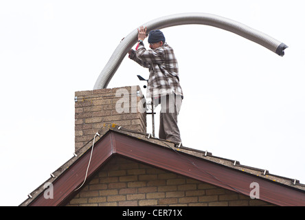 Man on house roof installing chimney liner for woodburning stove installation, Wales, UK Stock Photo