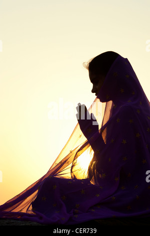 Indian teenage girl praying at sunset covered by a star veil. Silhouette. India Stock Photo