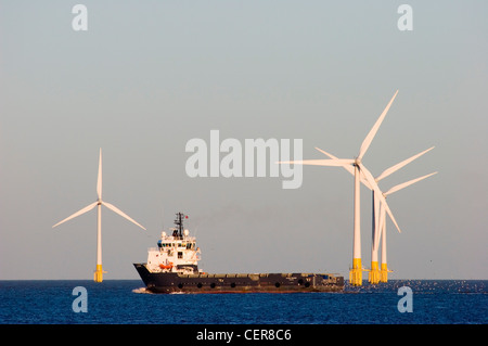 A cargo ship, the Olympic Provider passing in front of an offshore wind farm at Great Yarmouth in Norfolk. Stock Photo