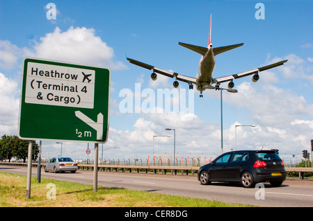 Cars on the A4 passing a road sign for Heathrow airport as a plane comes into land directly overhead. Stock Photo