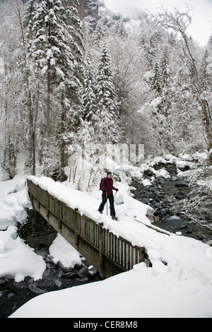 A woman walks across a snow-covered bridge using snowshoes near Sixt Fer A Cheval in the French Alps Stock Photo