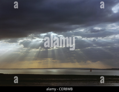 Sunlight streaming through dark storm clouds over the River Blackwater near Bradwell Waterside in Essex. Stock Photo