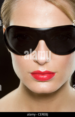 Female with blonde hair wearing worn tied up wearing bright red lipstick and large black sunglasses Stock Photo