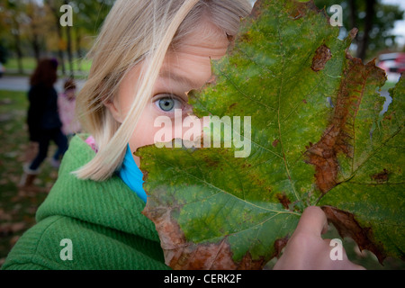 Ten year old girl peaking from behind a large leaf. Stock Photo