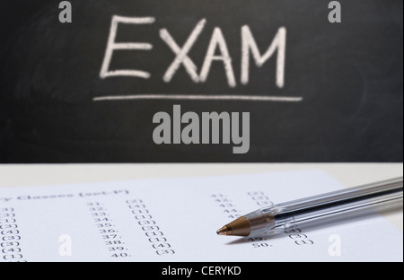 Close up on an exam paper and a pen with a blackboard in the background with EXAM written in chalk Stock Photo