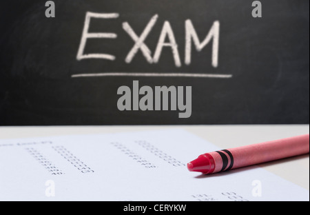 Close up on an exam paper and a red crayon with a blackboard in the background with EXAM written in chalk Stock Photo