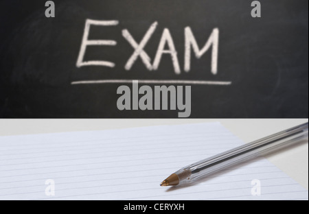 Close up on blank paper and a pen with a blackboard in the background with EXAM written in chalk Stock Photo