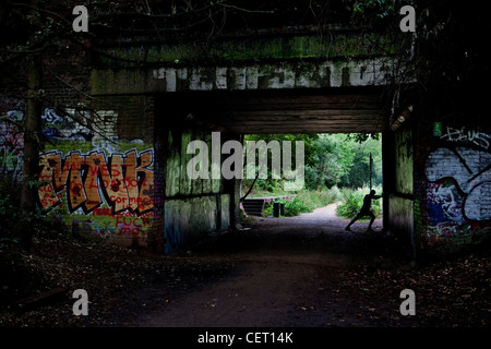 A jogger stretching underneath parkland walk bridge with graffiti on it Stock Photo