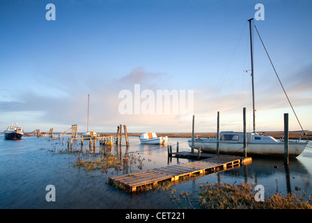 Boats moored at Thornham Harbour by the remains of an old pier at first light. Stock Photo