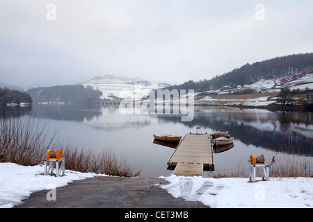 Small rowing boats tied to a jetty on Derwent reservoir following a winter snowfall in the Peak District National Park. Stock Photo
