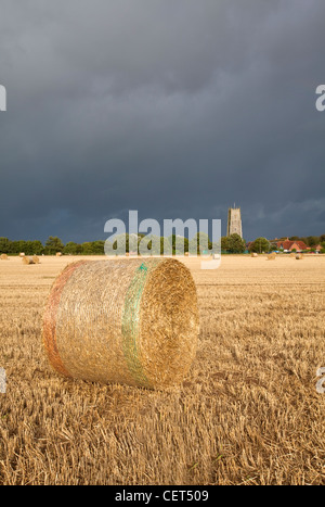 View over bales of hay towards stormy clouds over Holy Trinity and All Saints Church at Winterton-on-Sea. Stock Photo