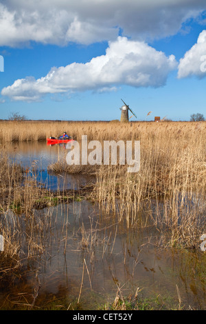 Canoeist on the River Thurne with the derelict Heigham Holmes Mill at Eelfleet Dyke in the distance on the Norfolk Broads. Stock Photo