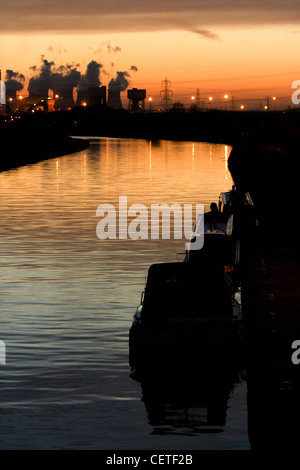 A view across water to smoke rising from industrial chimneys at sunset in Pontefract. Stock Photo