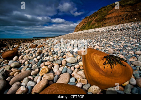 A view of red rocks on the pebble beach with cliffs in the background  at Seascale. Stock Photo