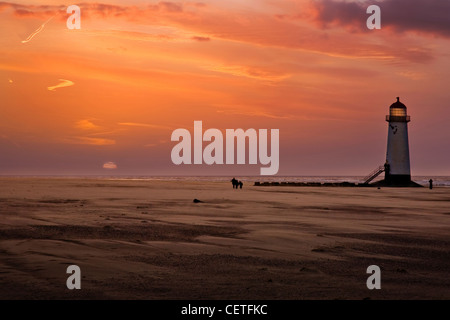 People walking on the beach beside Talacre Lighthouse at dusk. Stock Photo