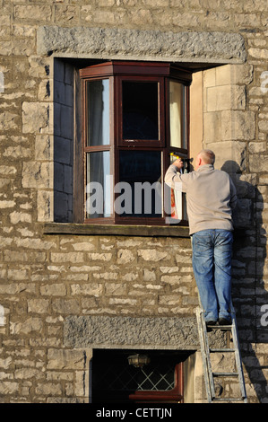 Man on ladder cleaning house windows. Lound Street, Kendal, Cumbria, England, United Kingdom, Europe. Stock Photo