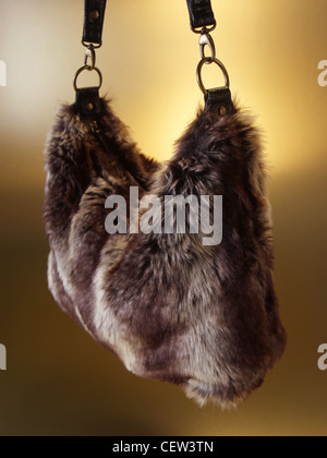 Brown faux fur handbag suspended by leather straps against a warm studio background, highlighting texture and winter fashion styling. Stock Photo
