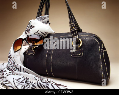 Black leather handbag styled with patterned scarf and sunglasses, photographed in studio against a neutral background. Stock Photo