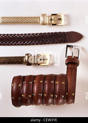 Flat lay of brown leather belts and studded leather bracelets arranged in parallel rows on a clean white background, showing different textures, braid Stock Photo