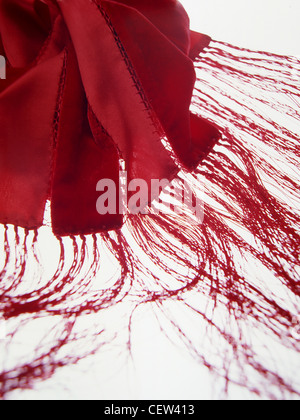 Close-up abstract detail of a red fringed scarf or shawl, showing flowing textile fibres and stitched fabric edges against a bright white background, Stock Photo