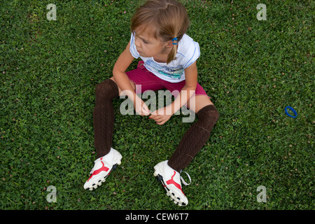 Six year old girl sitting in grass wearing soccer cleat and shin guards. Stock Photo