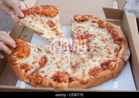 A child's hand grabbing a slice of pizza from a cardboard box. Stock Photo