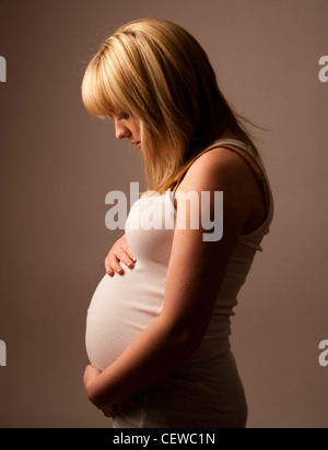 a profile of a pregnant young teenage blonde haired girl young woman holding her belly and looking down Stock Photo