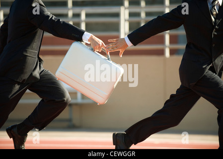Businessmen running in relay race, handing off briefcase Stock Photo
