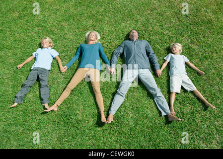 Family with two children lying side by side hand in hand on lawn, high angle view Stock Photo