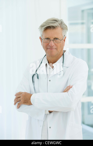 Senior grey-haired man doctor standing with serious expression holding ...