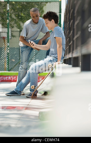 Young man using cell phone outdoors, friend watching Stock Photo