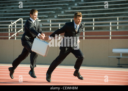 Businessmen running in relay race, handing off briefcase Stock Photo