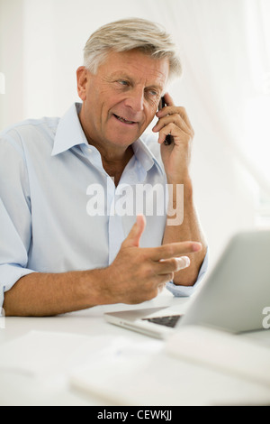 Man talking on cell phone while using laptop computer Stock Photo