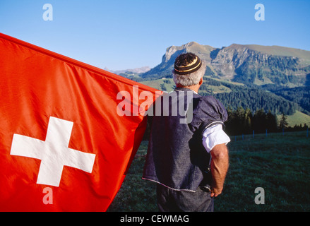 Elder in traditional costume holding the Swiss flag, admiring the Moleson mountain Stock Photo