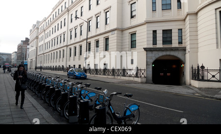 A woman walking past flats and a row of bicycle hire bikes at a docking station on William IV St. in London WC2 UK KATHY DEWITT Stock Photo