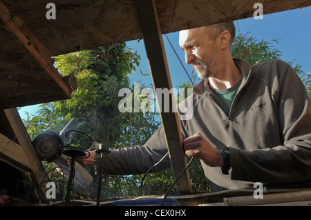 A man repairing the roof of his shed using a power tool Stock Photo