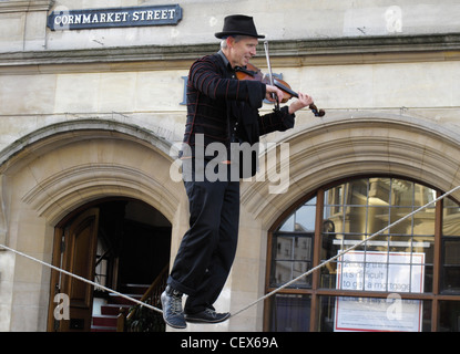 A man playing the fiddle balances on a tightrope outside a bank premises in Oxford High Street. England 2