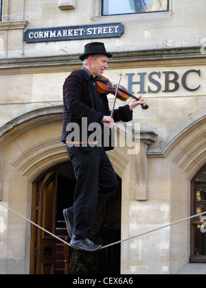 A man playing the fiddle balances on a tightrope outside a bank premises in Oxford High Street. England
