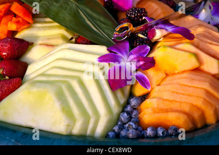 Tray of different seasonal and tropical fruit bright colors decorated with purple orchid blossoms Stock Photo