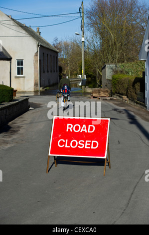 Man riding past Road Closed sign for flooding of River Spey at Garmouth, Scotland in April 2010 due to heavy snow melt. Stock Photo