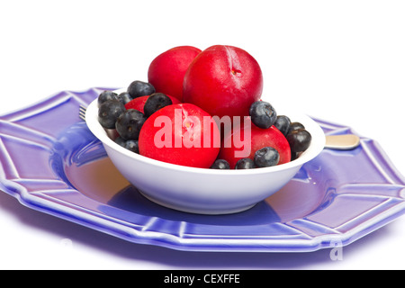 Fresh plums and blueberries in white bowl on white background Stock Photo