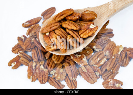 This spoon with Pecans in it is above other Pecans on a table Stock Photo