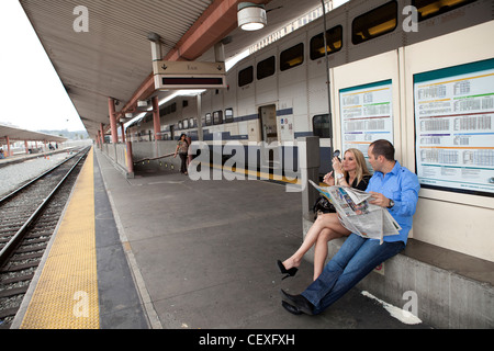 Couple sitting on train platform waiting for train Stock Photo