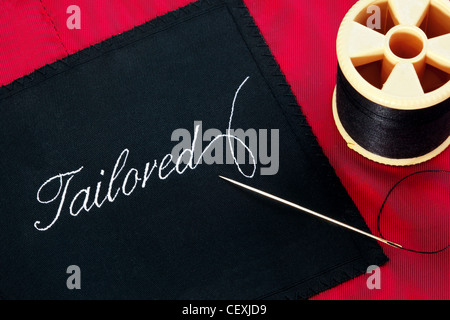 Photo of a garment label with the word Tailored on a red silk lining with a needle and reel of thread. Stock Photo