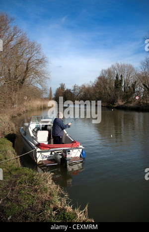 older man fishing from small boat on river waveney at geldeston norfolk uk Stock Photo